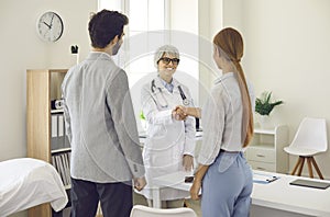 Young couple shaking hands with smiling family practitioner or pregnancy specialist