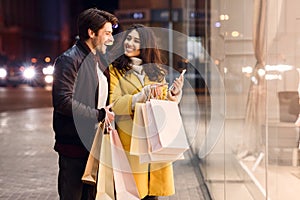 Young couple with shopping bags and smartphone near mall