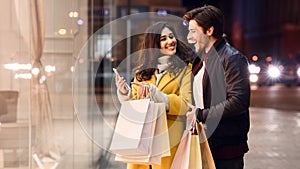 Young couple with shopping bags and smartphone near mall