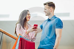 Young couple with shopping bags and smartphone talking in mall