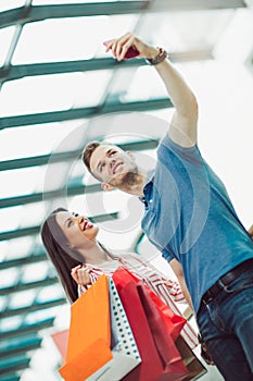 Young couple with shopping bags and smartphone talking in mall