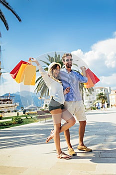 Young couple with shopping bags walking by the harbor of a touristic sea resort