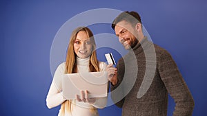 Young couple shopping online. Happy woman searching online shop on a tablet while man is paying with credit card