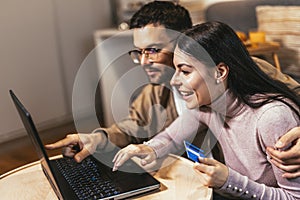 Young couple shopping together, customers paying by credit card online, sitting in cozy living room at home