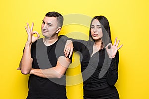 Young couple showing ok sign with and giving a thumb up gesture isolated over yellow background