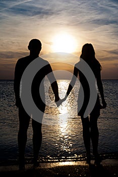 Young couple silhouette on a sea beach holding hands and lookin
