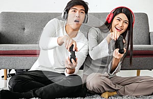 Young couple sit on floor having fun playing video games together in living room.
