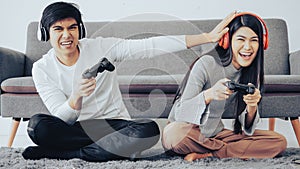 Young couple sit on floor having fun playing video games together in living room.
