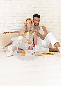 Young Couple Sit On Pillows Floor, Happy Hispanic Man And Woman Breakfast Tray Lovers In Bedroom