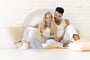 Young Couple Sit On Pillows Floor, Hispanic Man And Woman Using Tablet Computer Lovers Bedroom