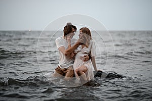 Young couple sits in the water on a rock and looks into each other& x27;s eyes