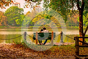 Young Couple sitting in an autumn park bench in Lakeshore. Falling in love in Maple leaf garden. Relaxation and romantic activity