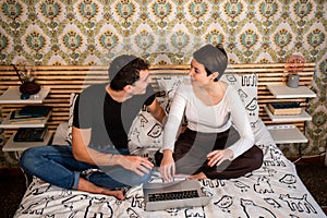 Young couple is sitting on the bed and using the computer.