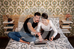 Young couple is sitting on the bed and using the computer.