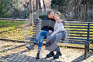 The young couple is sitting on a bench in the park in Rome.