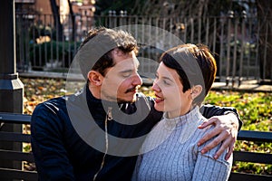 The young couple is sitting on a bench in the park in Rome.