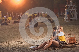 young couple sitting on blanket with straw basket on river beach