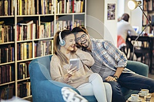 Young couple sitting in the cafe, drinking coffee and listening to music with smart phone