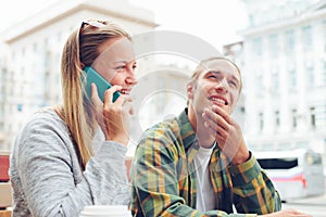 Young couple sitting in cafe with laptop and mobile phone, confused man and woman talking on the phone