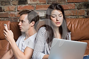 Young couple sitting on couch addicted obsessed with modern gadg photo