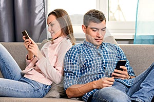 Young couple sitting on the couch in the room and use the mobile Internet for social networking. Communication problems.
