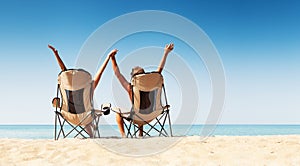 Young couple sitting in cozy chairs on the wild sea beach and re