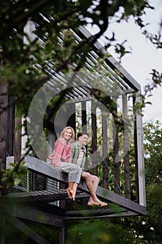 Young couple sitting and cuddling in hammock terrace in their new home in tiny house in woods, sustainable living