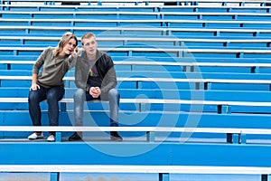 Young couple sitting on empty stadium sector on competition. Woman pointing and explaining the man with arms