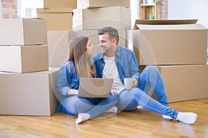 Young couple sitting on the floor around cardboard boxes using computer laptop, very happy moving to a new house