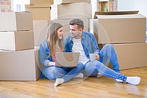 Young couple sitting on the floor around cardboard boxes using computer laptop, very happy moving to a new house