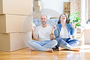 Young couple sitting on the floor arround cardboard boxes moving to a new house celebrating mad and crazy for success with arms