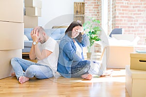 Young couple sitting on the floor arround cardboard boxes moving to a new house suffering from headache desperate and stressed