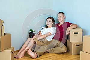 A young couple is sitting on the floor among the boxes. moved to a new house and happy. repair, mortgage, housewarming