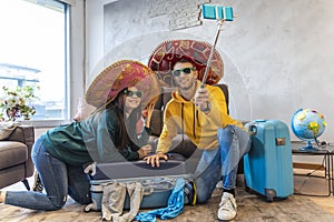 Young couple sitting on the floor at home takes a selfie wearing colorful sombrero