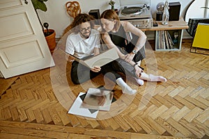 Young couple sitting on floor and listening music on vinyl player with different vinyl records