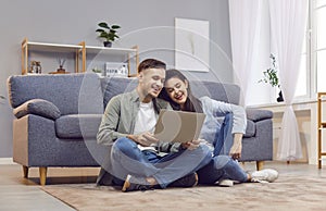 Young couple sitting on floor in living room at home using laptop for internet and social media