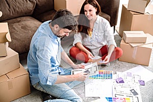 Young couple sitting on floor, looking at paint swatches guide palette