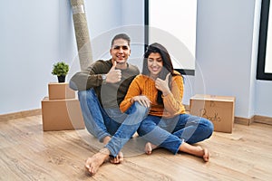 Young couple sitting on the floor at new home doing happy thumbs up gesture with hand