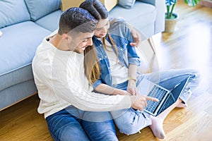 Young couple sitting on the floor of new home using computer laptop and smiling happy for moving to a new home