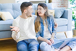 Young couple sitting on the floor of new home using computer laptop and smiling happy for moving to a new home