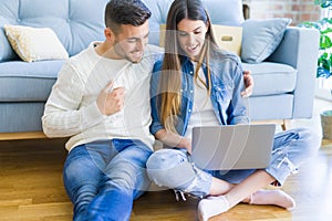 Young couple sitting on the floor of new home using computer laptop and smiling happy for moving to a new home