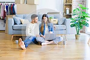 Young couple sitting on the floor of new home using computer laptop and smiling happy for moving to a new home