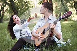 Young couple sitting in the forest and playing guitar, taking photo on old camera, summer nature, bright sunlight, shadows and gre