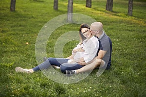 Young couple sitting in grass field in park. smiling happy, man kissing pregnant woman