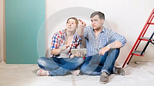 Young couple sitting in house under renovation and choosing places for new furniture