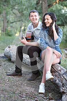 Young couple sitting on a log in the forest and playing guitar, summer nature, romantic feelings