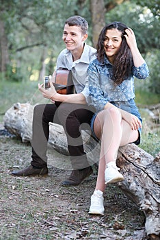 Young couple sitting on a log in the forest and playing guitar, summer nature, romantic feelings