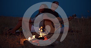 Young couple sitting near bonfire, man playing guitar. Romantic music and happy couple relationships. Romance couple