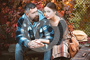Young couple sitting outdoors at the autumn park. Lifestyle, happy family on a sunny day. Girl and bearded guy or happy