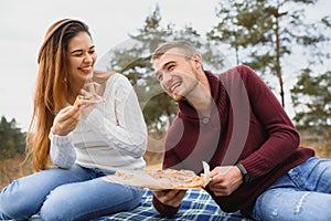 Young couple sitting on park bench and eating pizza.Fast food.Woman and man having picnic at sunset. Guys relaxing and enjoying